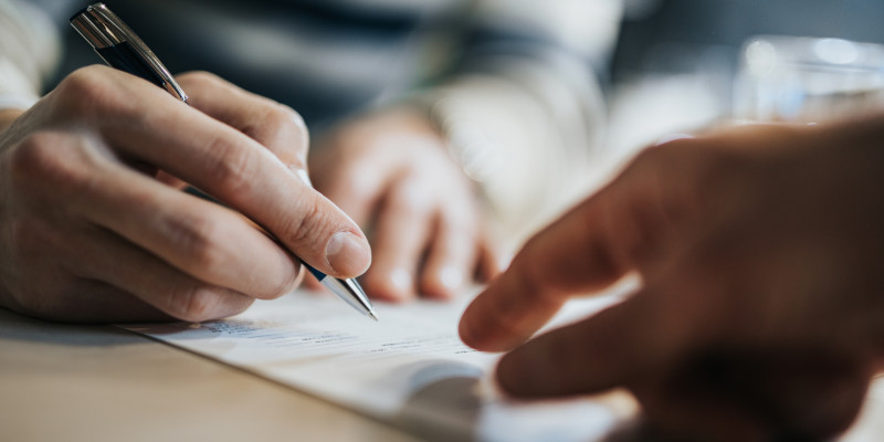 Close up of unrecognizable man signing a contract while financial advisor is aiming at the place he need to sign.